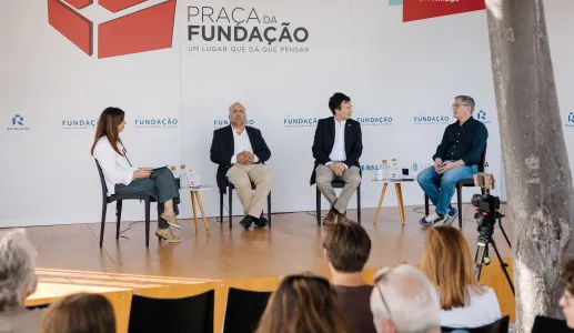 Quatro pessoas em palco, sentadas em cadeiras pretas, a falar com plateia a assistir. Logo e texto "Praça da Fundação".