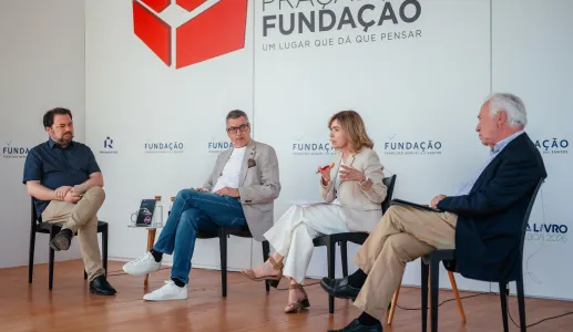 Quatro pessoas sentadas em cadeiras pretas, a debater entre si. Ao fundo, o texto "Praça da Fundação"