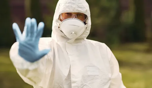 Imagem de uma pessoa, vestida com um fato de segurança branco, máscara, óculos e luvas azuis.