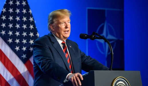 Donald Trump a falar, num púlpito. Fundo azul, com uma bandeira dos EUA e o símbolo da Nato. Créditos: Gints Ivuskans/shutterstock