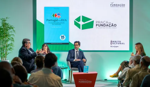 Imagem de quatro pessoas a conversar perante uma plateia,  sob um fundo verde.