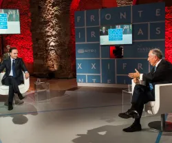 Dois homens, um deles Marcelo Rebelo de Sousa, sentados em cadeiras conversam num palco iluminado, com o texto "FRONTEIRAS XXI" ao fundo.