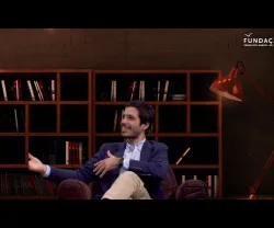 O podcaster José Maria Pimentel sentado num sofá, com uma estante de livros ao fundo.