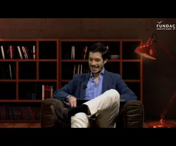 Homem sorridente em sofá, com prateleira de livros atrás. Logo da Fundação no canto superior direito.