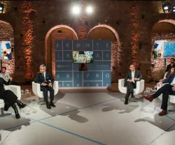 Debate com quatro participantes sentados cadeiras. Ao fundo, um painel com o texto "Fronteiras XXI". 