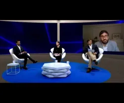 Três pessoas sentadas em cadeiras brancas num estúdio, uma outra aparece no ecrã ao fundo.
