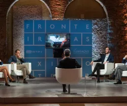 Debate num estúdio de televisão com cinco oradores, sentados em cadeiras brancas. Ao fundo, o texto "FRONTEIRAS XXI".