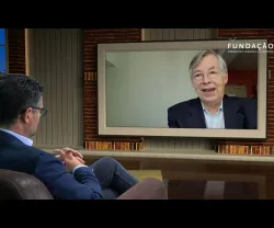 O jornalista Pedro Pinto, num estúdio de televisão, a olhar para uma tela que mostra François Heisbourg a falar.