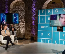 Debate com duas pessoas num estúdio de televisão; texto "FRONTEIRAS" e "XXI" visível.