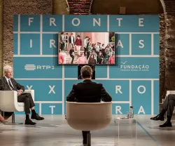 Painel de discussão com quatro pessoas, fundo azul com "FRONTEIRAS XXI". Televisão em exibição.