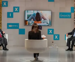Debate em estúdio com apresentadora e dois convidados, imagem de fundo com pessoa abatida.
