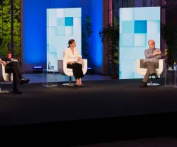 Painel de discussão com cinco pessoas sentadas, num ambiente iluminado e decorado.