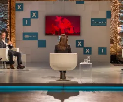Um painel de discussão com quatro pessoas sentadas e uma tela ao fundo com fumo vermelha.