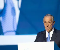 Marcelo Rebelo de Sousa a discursar num púlpito branco. Está vestido com um fato preto e uma gravata azul.