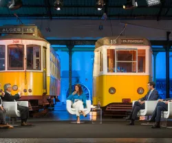 Painel de discussão com quatro pessoas sentadas em cadeiras brancas, entre dois elétricos amarelos.