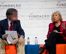 Dois palestrantes numa mesa redonda. Fundo com a palavra "FUNDAÇÃO" repetida.