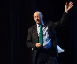 Richard Baldwin a discursar, com uma mão levantada, sobre um fundo escuro, ligeiramente iluminado. 
