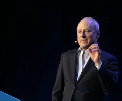 O filósofo Michael Sandel a falar, de pé, com um microfone sem fios, sobre um fundo preto. 
