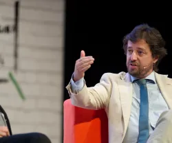 Dois homens em debate. Um gesticula enquanto fala, sentado numa cadeira vermelha.