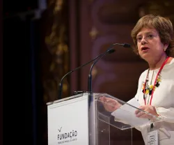 Mulher a falar num púlpito, com o texto "FUNDAÇÃO" visível. 