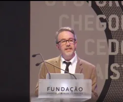 Homem a fazer uma apresentação em palco, num púlpito que tem o logo da Fundação.