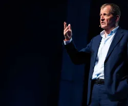 Alastair Campbell em palco, gesticulando enquanto fala ao microfone.
