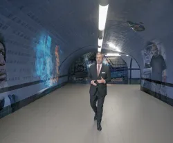 O jornalista Carlos Daniel a andar num túnel com murais de rostos e texto nas paredes.