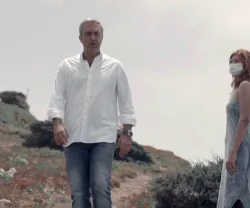 O jornalista Carlos Daniel a passar ao lado de uma mulher, que usa uma máscara. Céu nublado ao fundo.