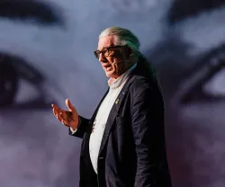 Howard Williamson, professor de Política Europeia, a falar de pé, gesticulando, sobre um fundo de dois olhos gigantes.