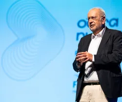 Um homem, Jaime Gama, a falar ao microfone em palco, com fundo azul e texto "outra vez nunca mais".