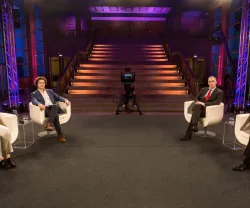 Quatro pessoas sentadas em cadeiras brancas num palco com escadas iluminadas ao fundo.