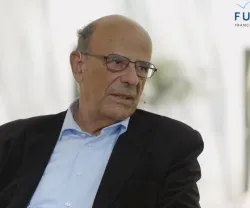 Homem mais velho com óculos, sentado, a falar. Logo da Fundação no canto superior direito.