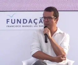 O ilustrador Pedro Vieira, sentado, a falar para um microfone que tem na mão. Ao fundo, um painel com o texto "Fundação Francisco Manuel dos Santos".