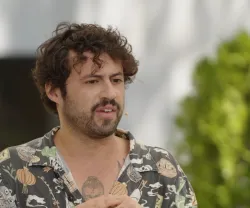 Retrato de Diogo Faro, com cabelo encaracolado, camisa estampada, a falar na rua.