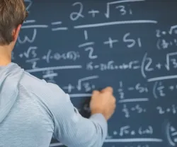 Um homem escreve fórmulas matemáticas num quadro negro.