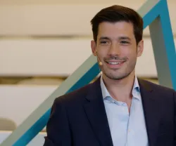 Homem sorridente, de fato, com um microfone, num espaço moderno.