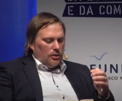 Homem de cabelo comprido e barba lê a ler num palco. Logotipo "FUNDAÇÃO FRANCISCO MANUEL DOS SANTOS".