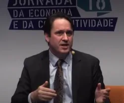 Homem, de fato preto, a falar em palco. Texto ao fundo: "JORNADA DA ECONOMIA E DA COMPETITIVIDADE".