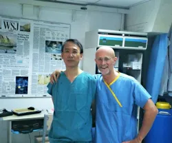 Os cirurgiões Xiaoping Ren e Sergio Canavero sorridentes posam para uma fotografia, num ambiente hospitalar.