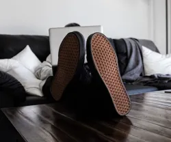 Pés pousados em cima de uma mesa de uma pessoa que está recostada no sofá.
