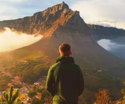 Homem de costas olha para uma montanha com neblina ao amanhecer.