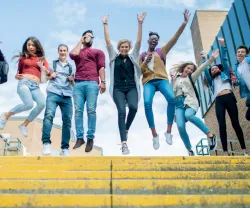 Grupo de jovens a saltar numas escadas amarelas, todos a sorrir.