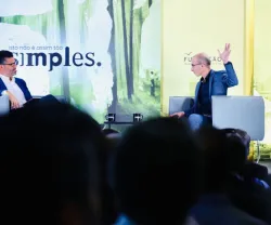 Harari e o jornalista Pedro Pinto conversam num evento ao vivo; um levanta a mão. Texto: "isto não é assim tão simples."