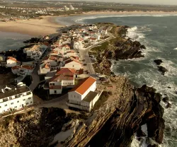 Vista aérea de uma aldeia costeira com casas de telhados laranja junto ao mar.
