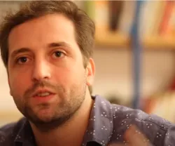 O humorista brasileiro Gregório Duvivier a falar, com uma estante de livros ao fundo.