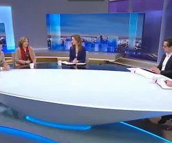 Quatro pessoas sentadas à volta de uma mesa oval Num estúdio de televisão.