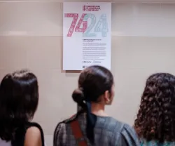 Três raparigas estudantes a ver um cartaz que tens os números "74" e "24" em destaque.