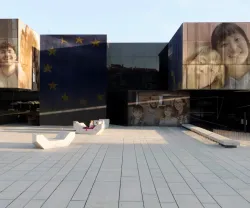 Edifício moderno com rostos de várias pessoas e estrelas da União Europeia nas fachadas.