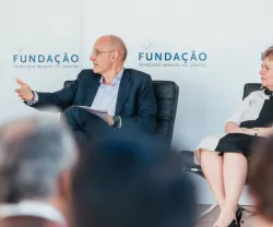 Dois oradores em palco, sentados. Um a falar e outro a ouvir. Fundo com logotipos da Fundação.