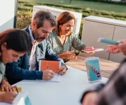 Dois homens e uma mulher sentados a dar autógrafos, a sorrir enquanto interagem com as pessoas.